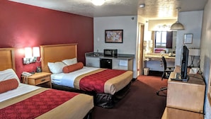 Habitación de hotel con dos camas, un escritorio, una computadora, un microondas y una kitchenette pequeña.