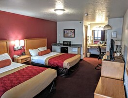 A hotel room with two beds, a desk, a computer, a microwave, and a small kitchenette.