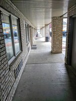 A covered walkway with brick walls and large windows, leading to a parking area.