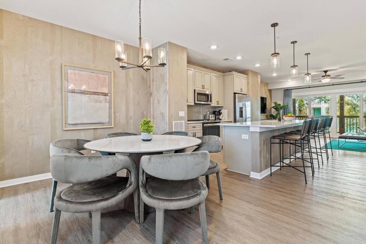 A modern kitchen with a central island, grey upholstered chairs, and pendant lighting.