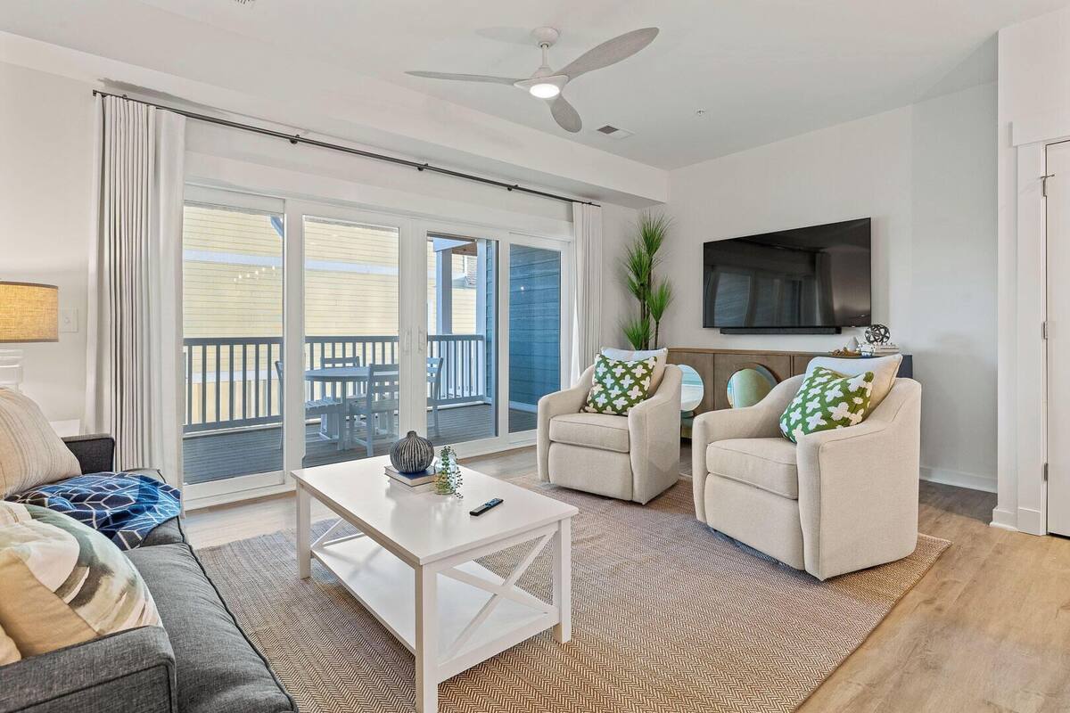 A living room with a sofa, two armchairs, a coffee table, a TV, and a balcony with a view.