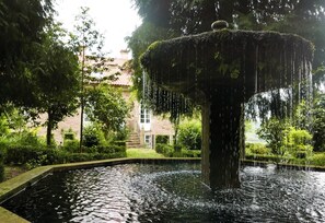 A fountain in a garden with a building in the background. - Hotel Pazo de Bieite (Boimorto)
