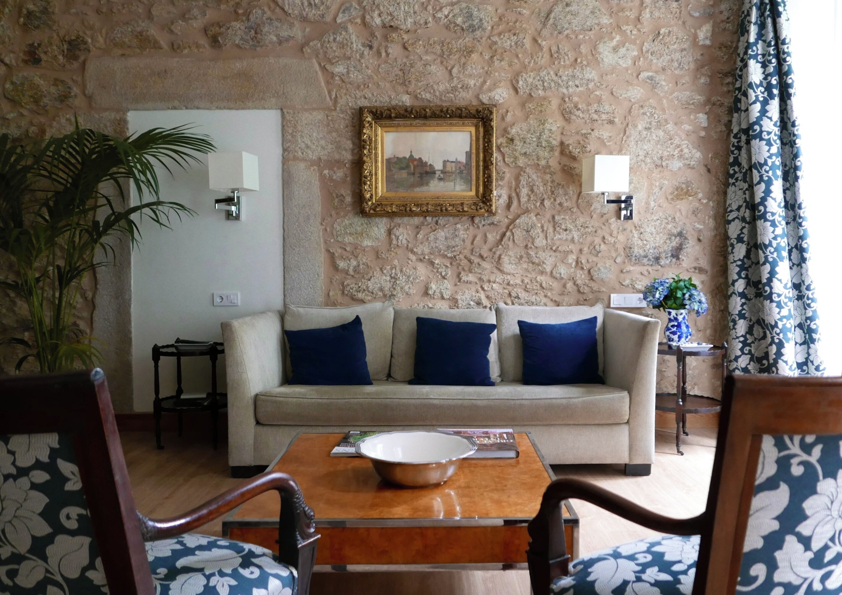 A living room with a stone wall, a sofa with blue cushions, a wooden coffee table, and a chair with a floral pattern.