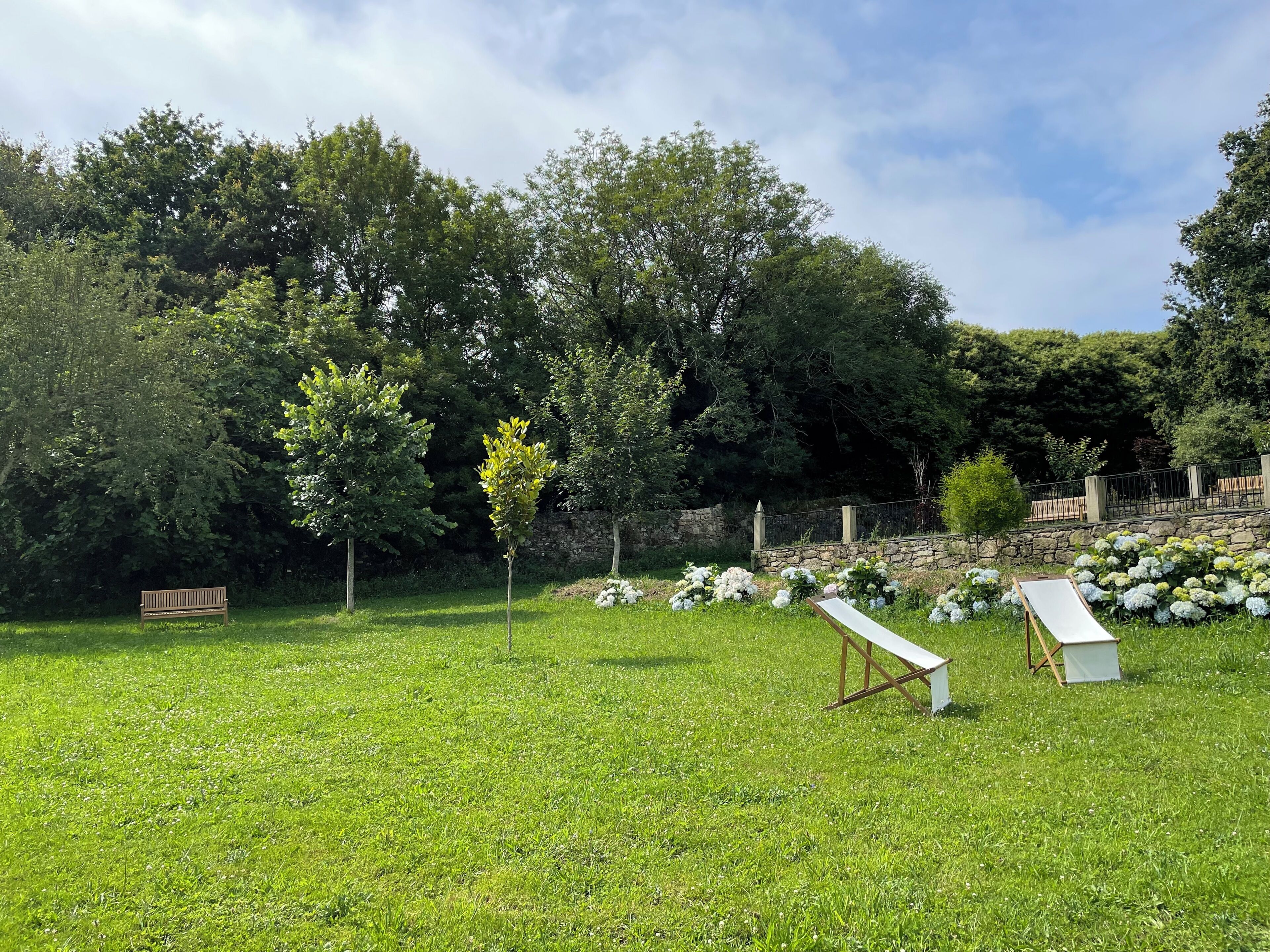 A grassy outdoor area with a bench, a small table, and a stone wall in the background.