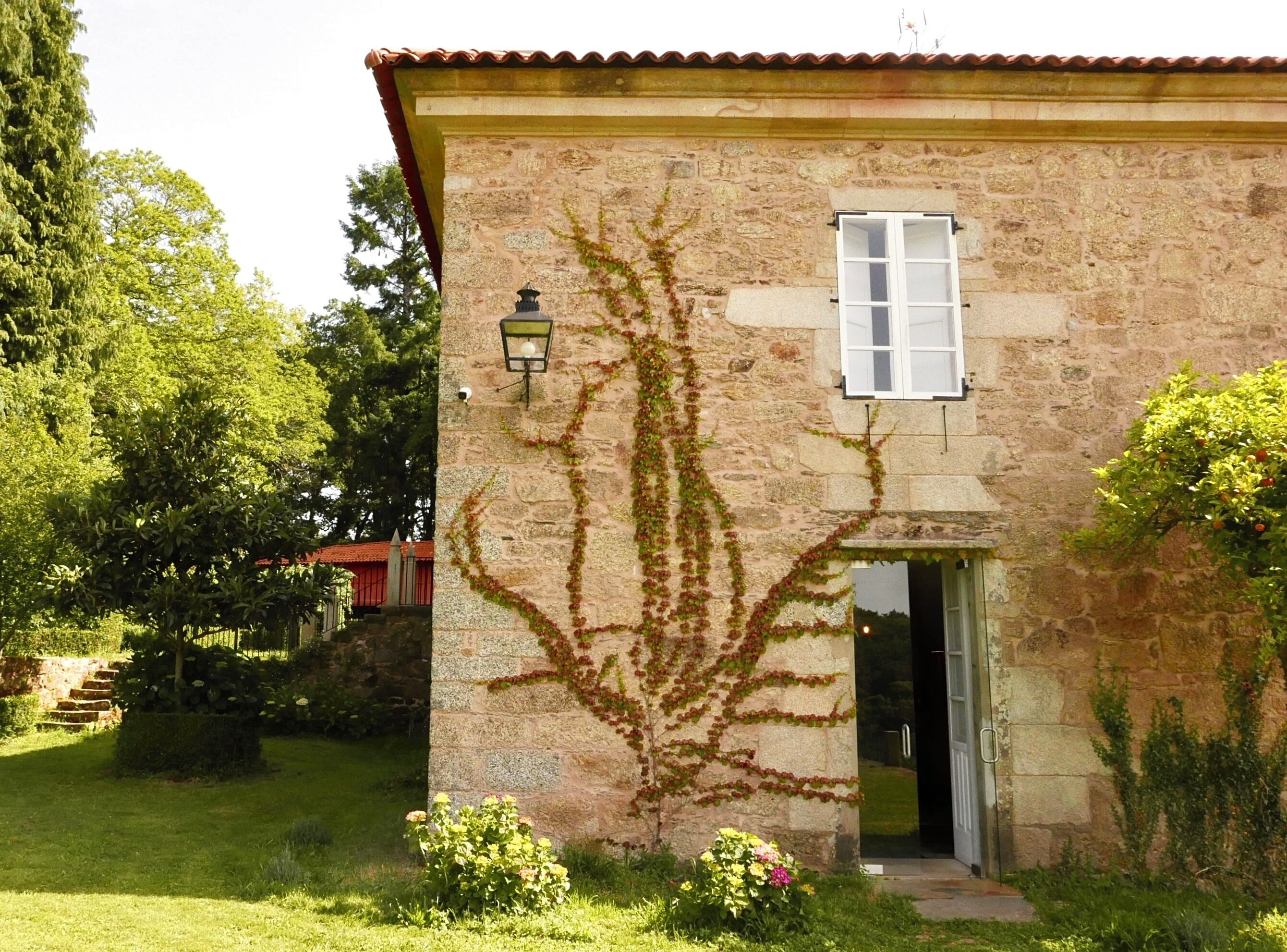 A stone building with a window and a door, surrounded by greenery.