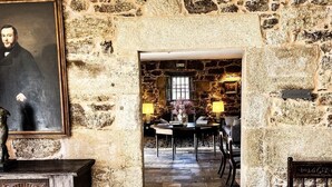 Une pièce aux murs de pierre, comprenant un coin repas, un portrait encadré et un banc en bois.