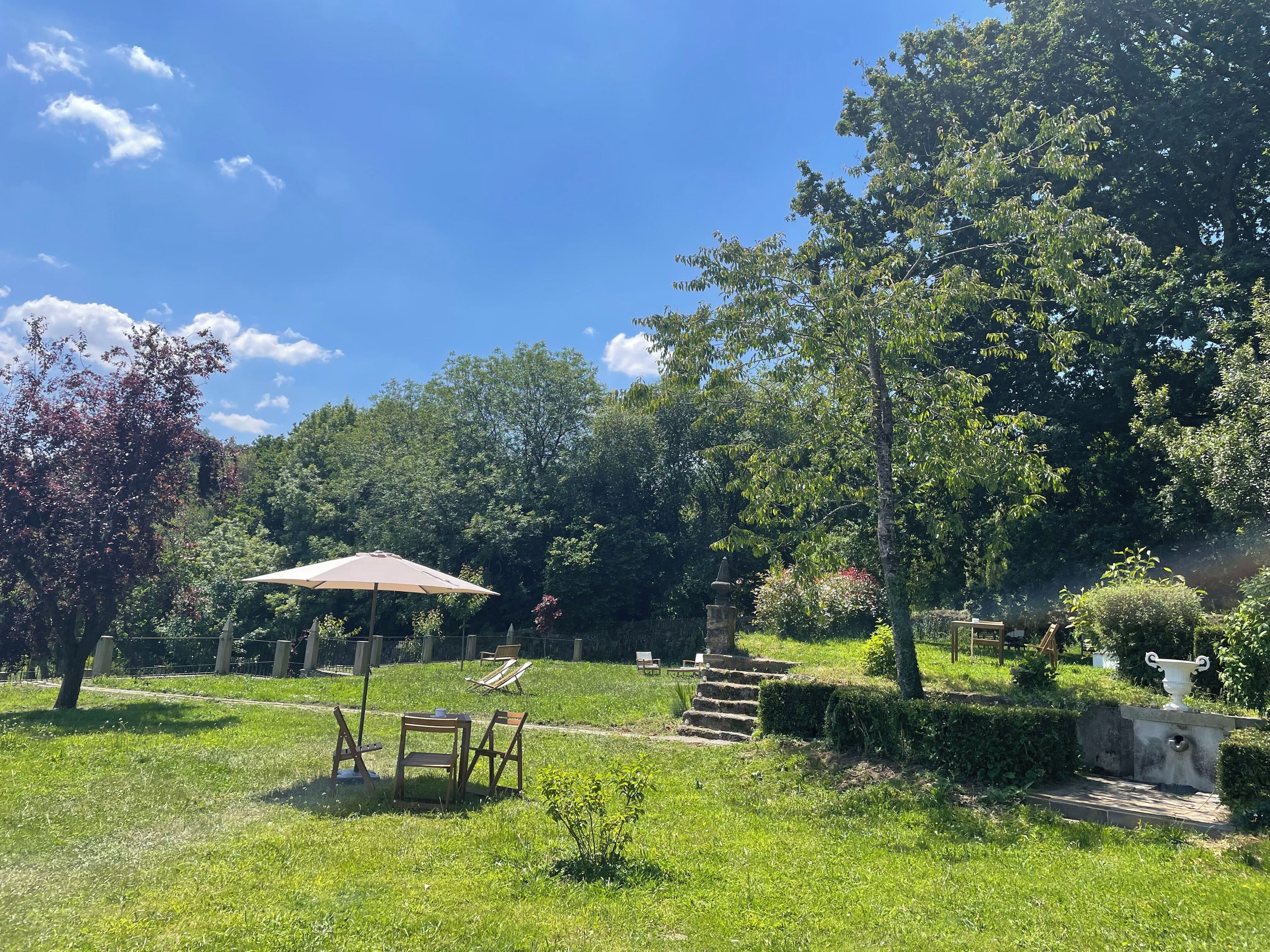 A garden with a table and chairs, a stone fountain, and a tree.