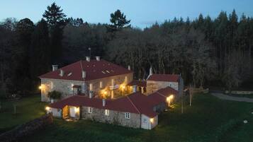 A large stone building with multiple red-roofed structures, surrounded by a forested area.