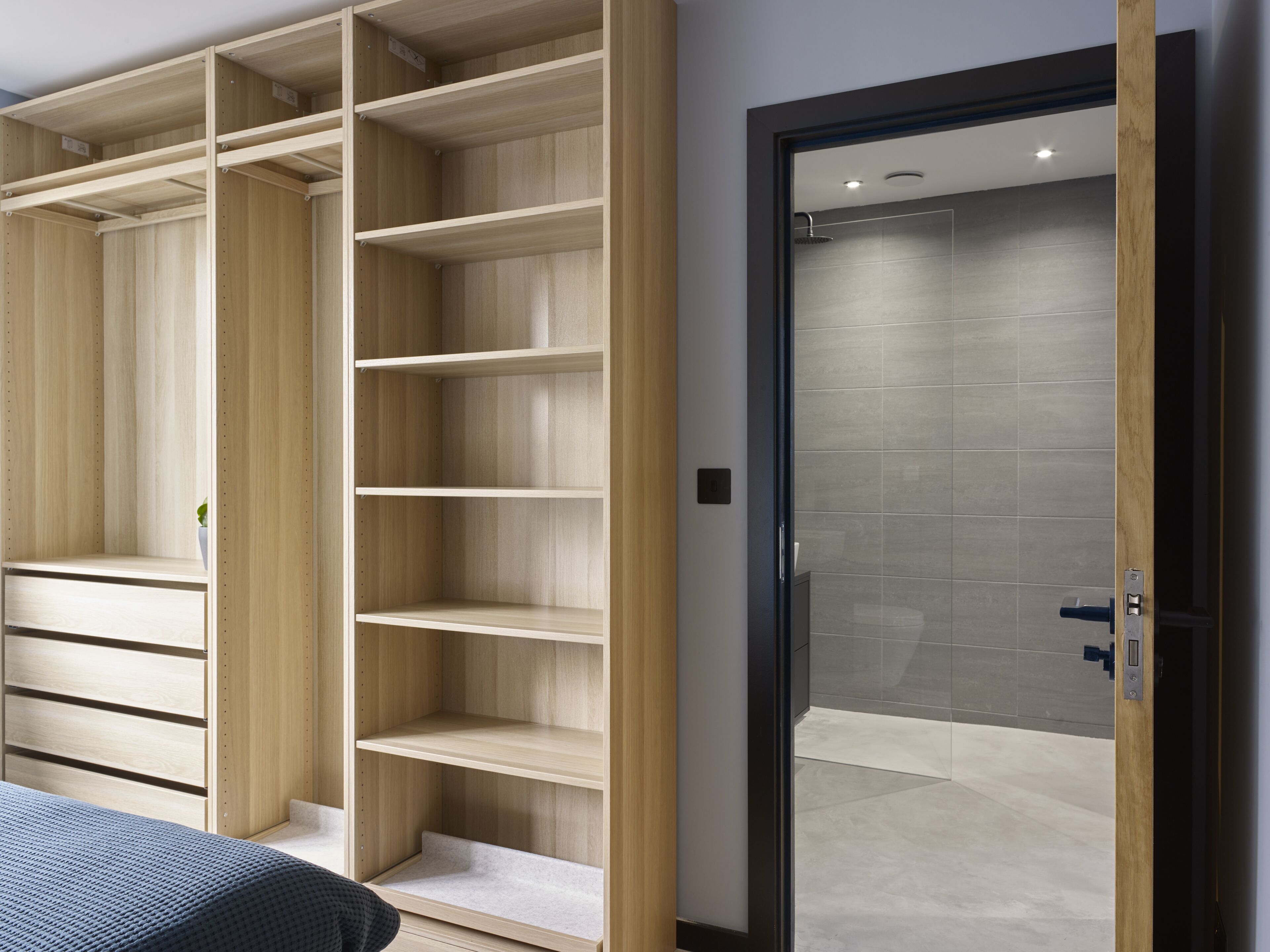 A modern bedroom with built-in wooden shelving, a glass shower door, and a bed with a blue blanket.