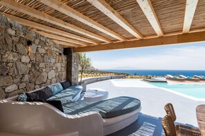 Un área de estar exterior moderna con una pared de piedra, techo de madera y vista al océano.