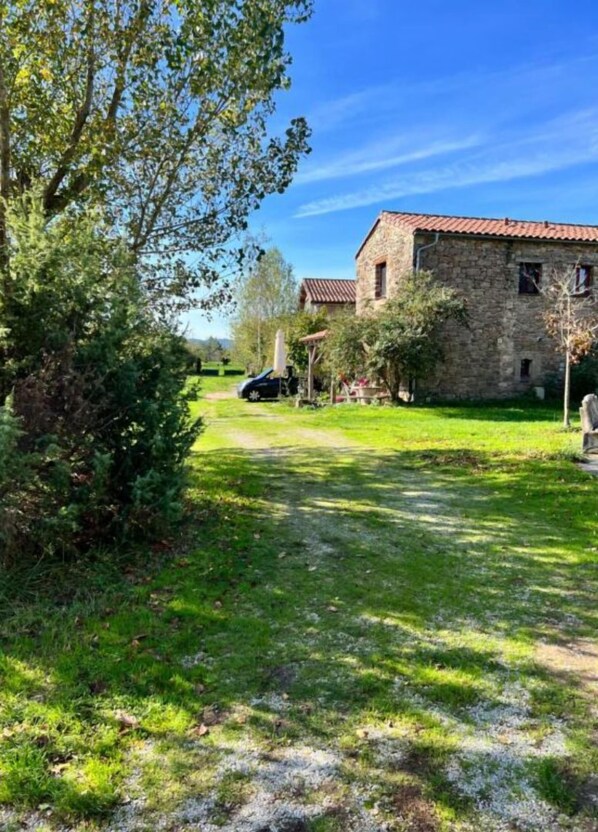A stone building with a red-tiled roof, surrounded by a grassy area and trees. - Gite Écureuil, 3 Personnes (Avène)