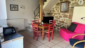 Een gezellige kamer met een eettafel, stoelen, een roze bank, een televisie en een stenen muur.