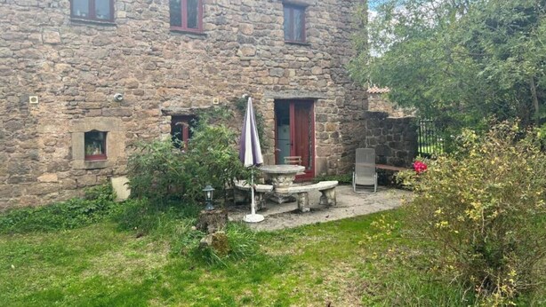 Een stenen huis met een kleine tuin, een tafel en een stoel buiten.