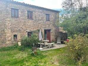 A stone house with a small garden, a table, and a chair outside. - Gite Écureuil, 3 Personnes (Avène)