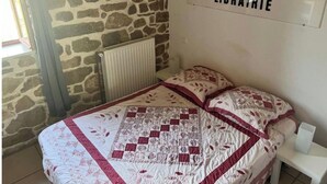Een slaapkamer met een stenen muur, een radiator, een gewatteerde spreideken en een bordje met de tekst 'LIBRAIRIE'.