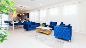 A modern living room with blue sofas, a coffee table, and a dining area with chairs. - 3312 LW 5-BR Luxury Villa with Pool Disney Delight (Four Corners)