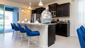 A modern kitchen with dark cabinets, a granite countertop, and blue bar stools. - 3312 LW 5-BR Luxury Villa with Pool Disney Delight (Four Corners)