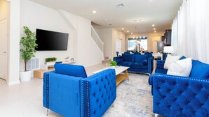 A modern living room with blue sofas, a flat-screen TV, and a staircase leading to another level. - 3312 LW 5-BR Luxury Villa with Pool Disney Delight (Four Corners)