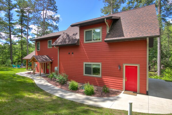 A red two-story house with a covered porch, a red door, and a well-maintained lawn. - Amazing River House with covered patio! Sleeps 10-14. Kayaks,Fireplace,Games. (Colfax)