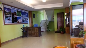 A reception area with a framed travel information poster, a reception desk, a staircase, and a large pot of marigold flowers.