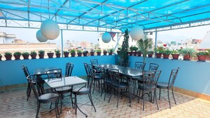 An outdoor patio with a blue ceiling, multiple tables and chairs, potted plants, and a view of the cityscape.