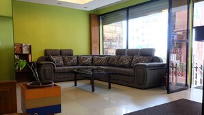 A living room with a sectional sofa, a coffee table, a bookshelf, and a potted plant.