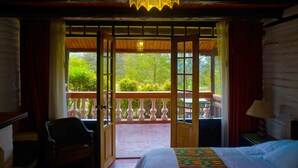 A room with a bed, a chair, a balcony with a railing, and a view of greenery outside.