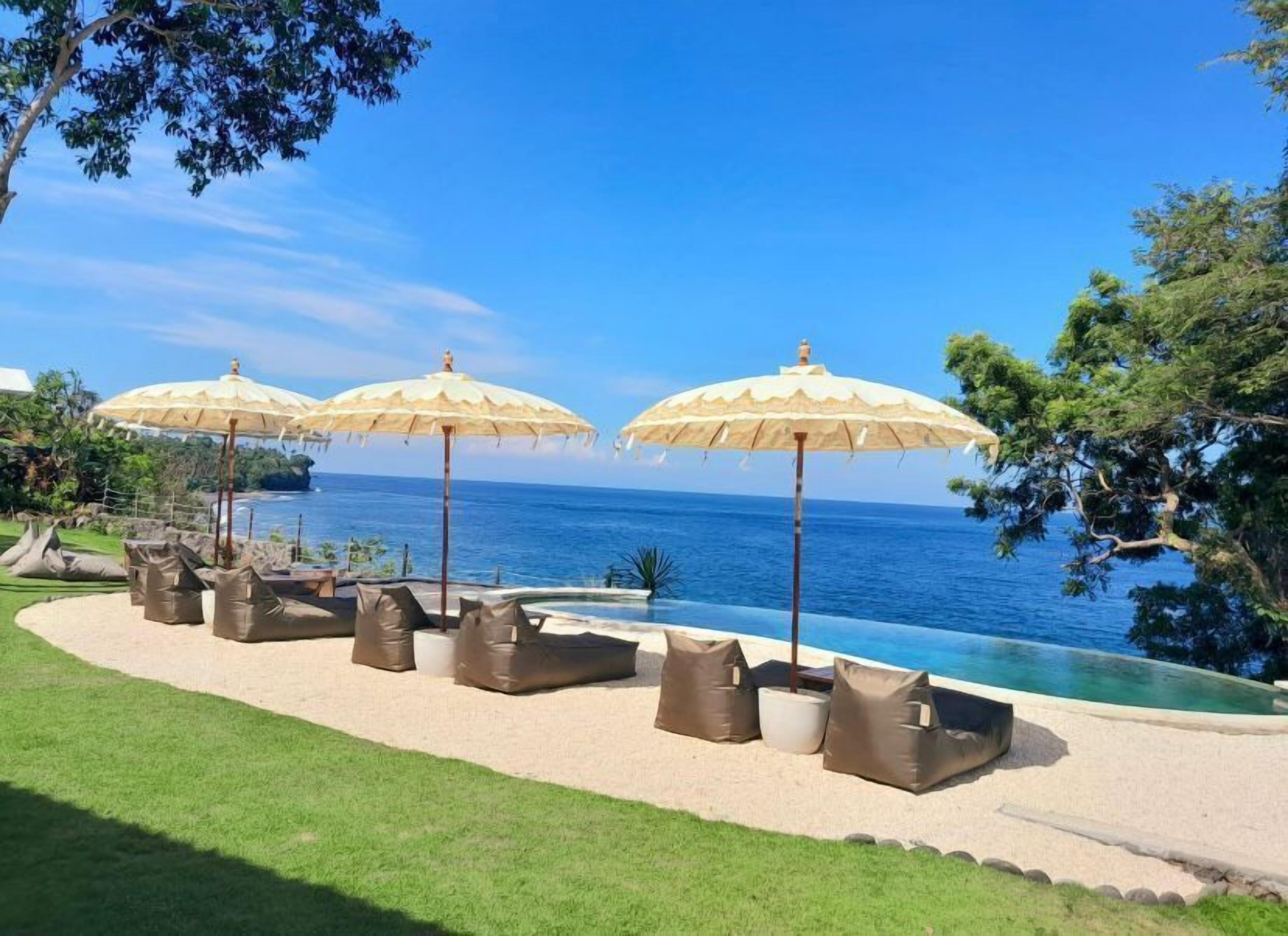 A poolside area with lounge chairs and umbrellas, overlooking a clear blue sea.