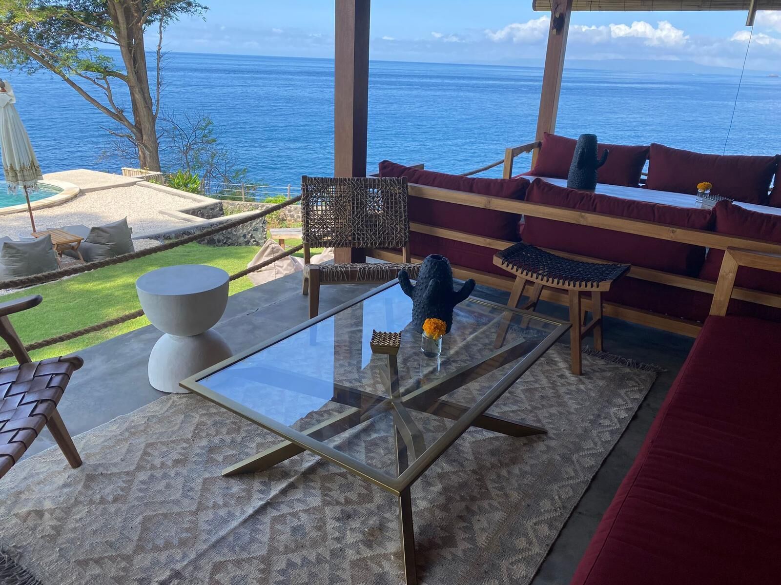 A modern outdoor seating area with a glass table, red cushioned sofas, and a view of the ocean.