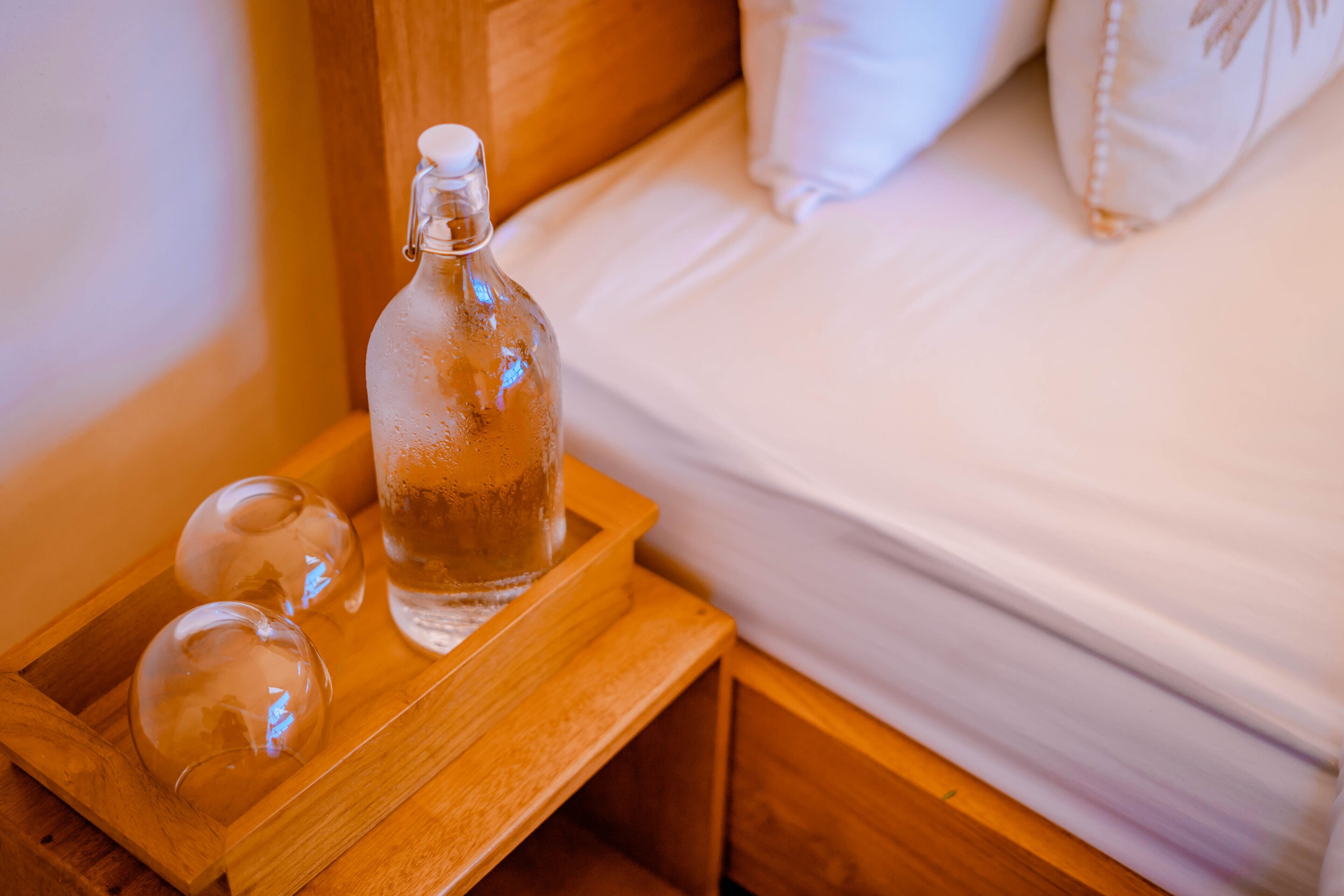 Ein Nachttisch aus Holz mit einer Glasflasche und zwei klaren Glaskugeln.