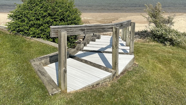 A wooden staircase leading to a beach with a clear view of the water and distant land.