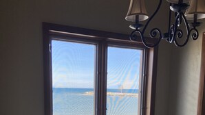 A room with a large window overlooking a beach, a white table, and a chandelier.