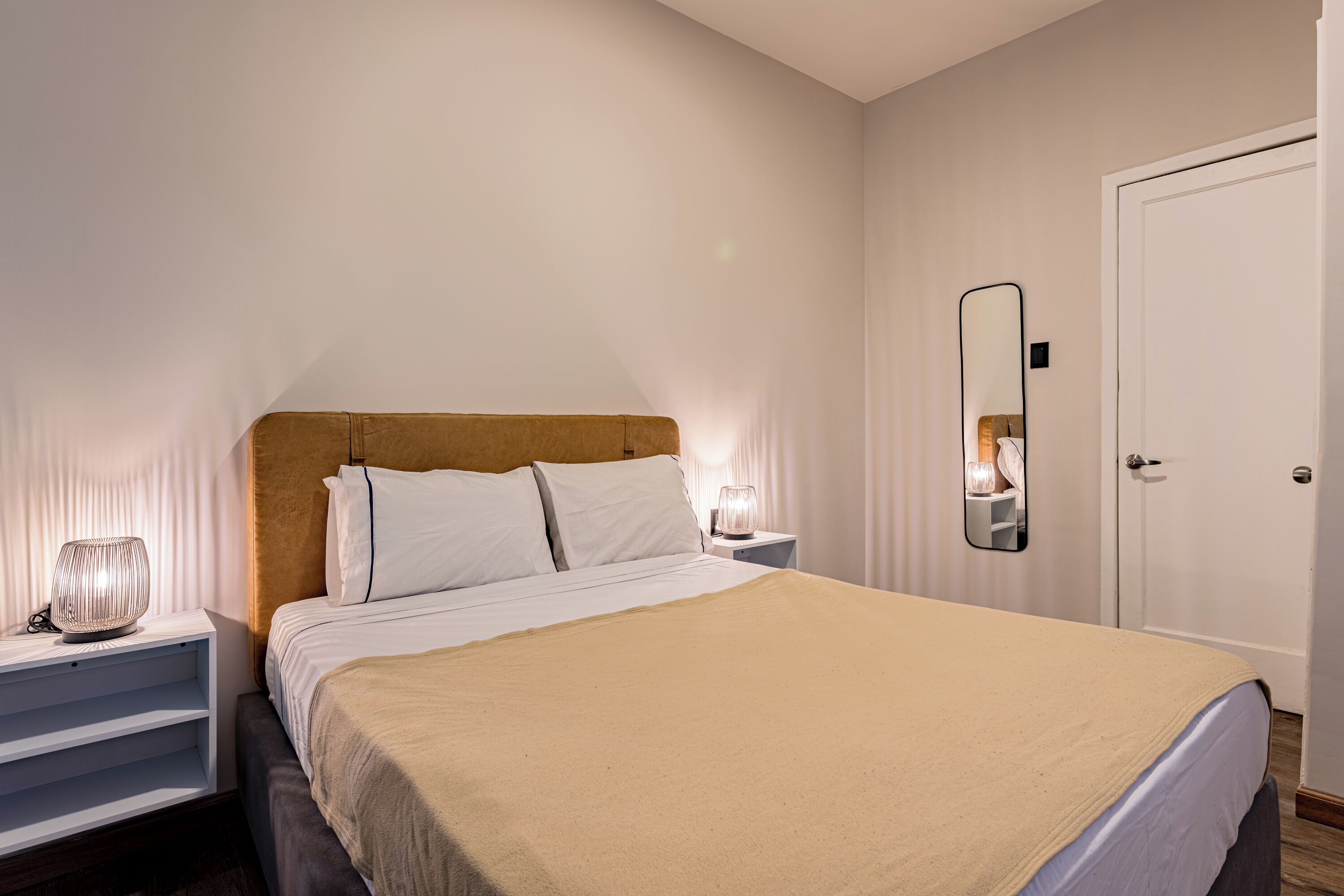 A neatly made bed with a headboard, bedside tables with lamps, a mirror, and a door.