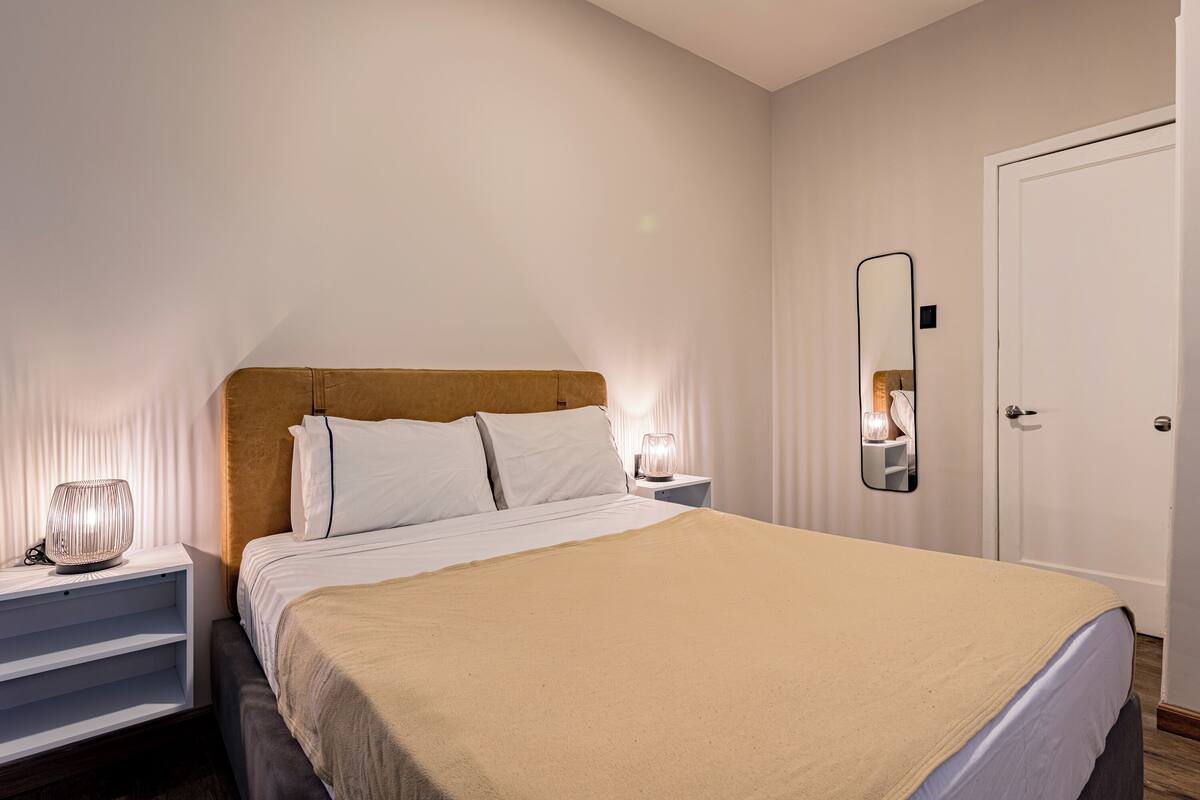 A neatly made bed with a headboard, bedside tables with lamps, a mirror, and a door.