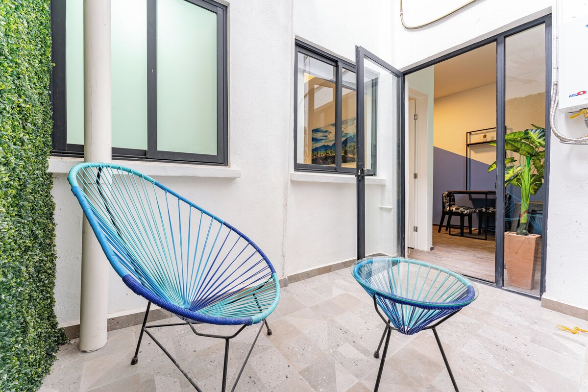 A room with two blue wire-framed chairs, a white wall, a glass door leading to another room, and a potted plant.