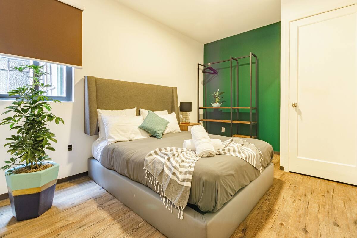 A bedroom with a bed, a potted plant, a nightstand, and a green wall.