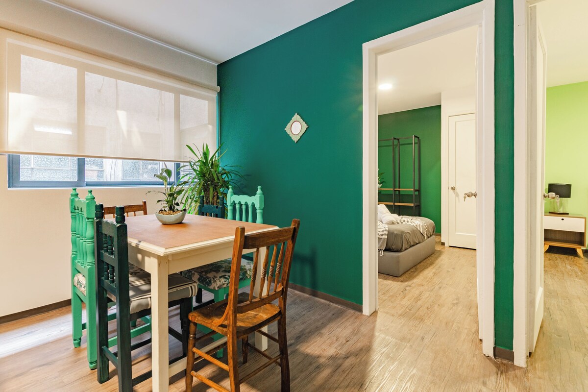 A dining area with a wooden table and chairs, a potted plant, and a window with blinds.