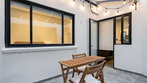 A small patio area with a wooden table and chairs, a window with a view, and a door leading to another room.