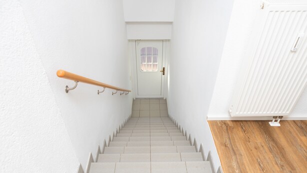 A staircase with a handrail, a door at the top, and a radiator on the right.