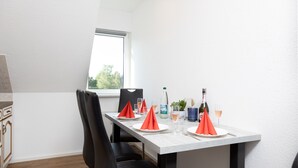 A dining area with a white table, black chairs, red napkins, and a bottle of champagne.