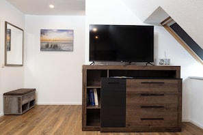 A modern living room with a flat-screen TV, a bookshelf, and a bench.