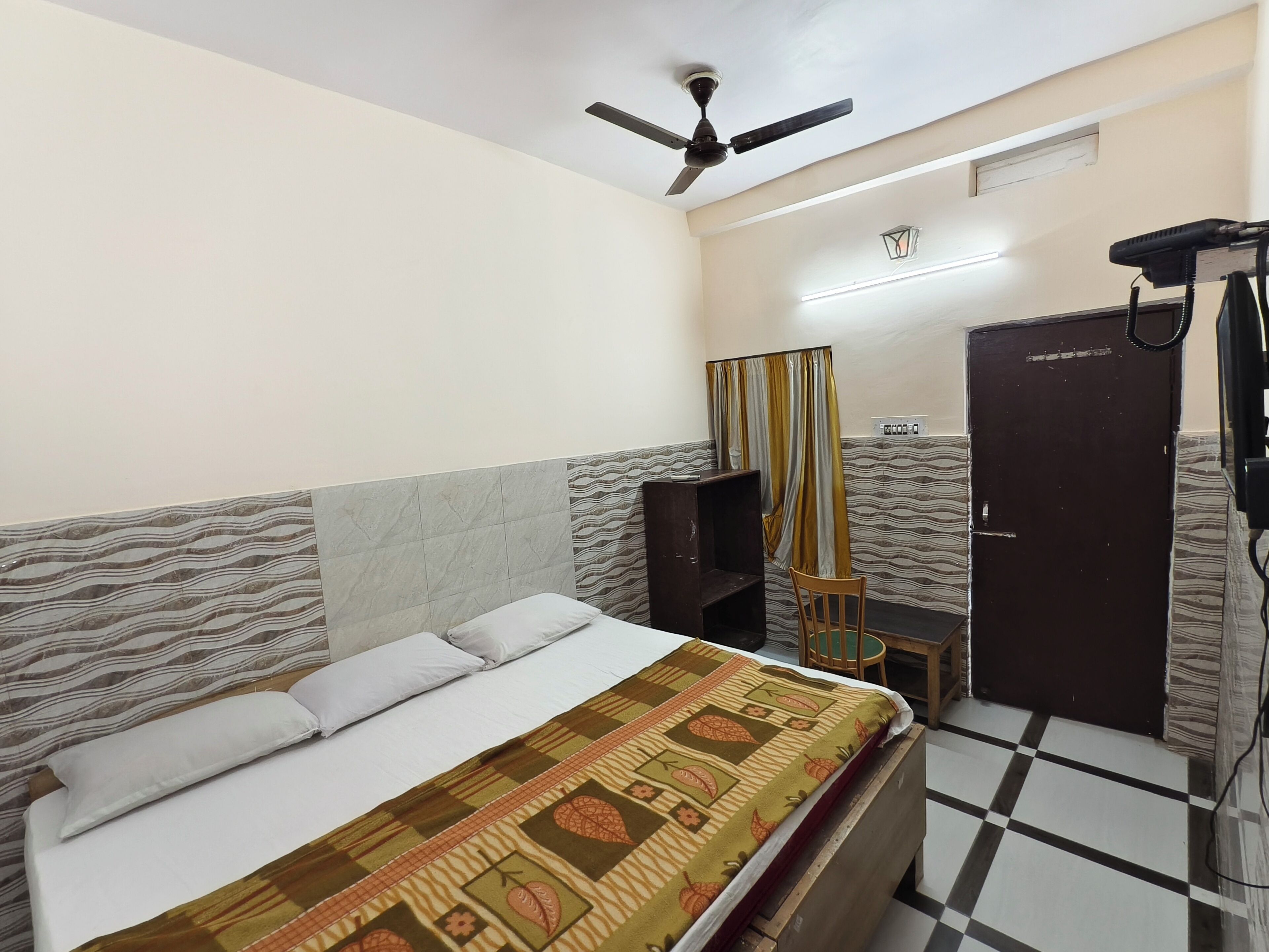 A bedroom with a bed, a ceiling fan, a wardrobe, and a small table.