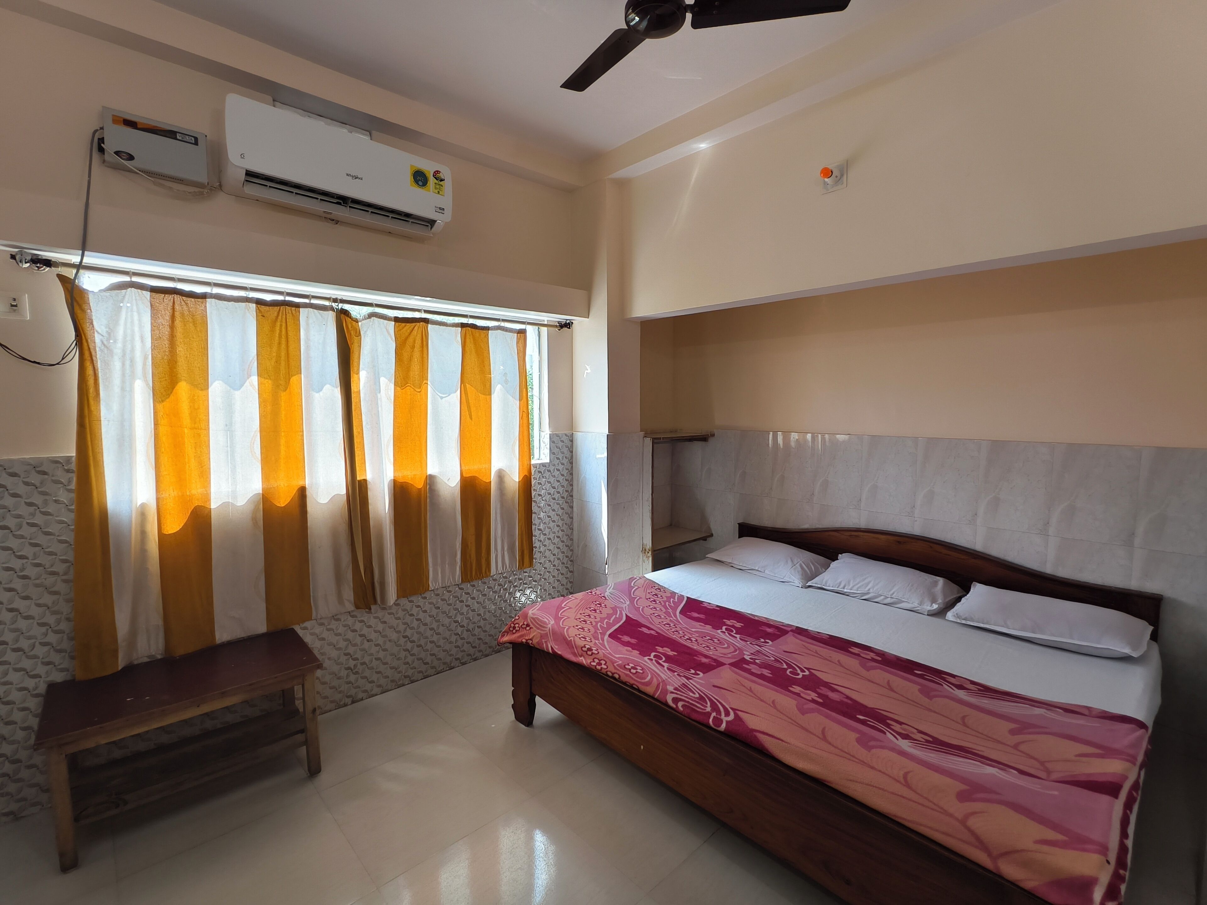 Une chambre à coucher avec un lit, un ventilateur de plafond, un climatiseur et une fenêtre avec des rideaux.
