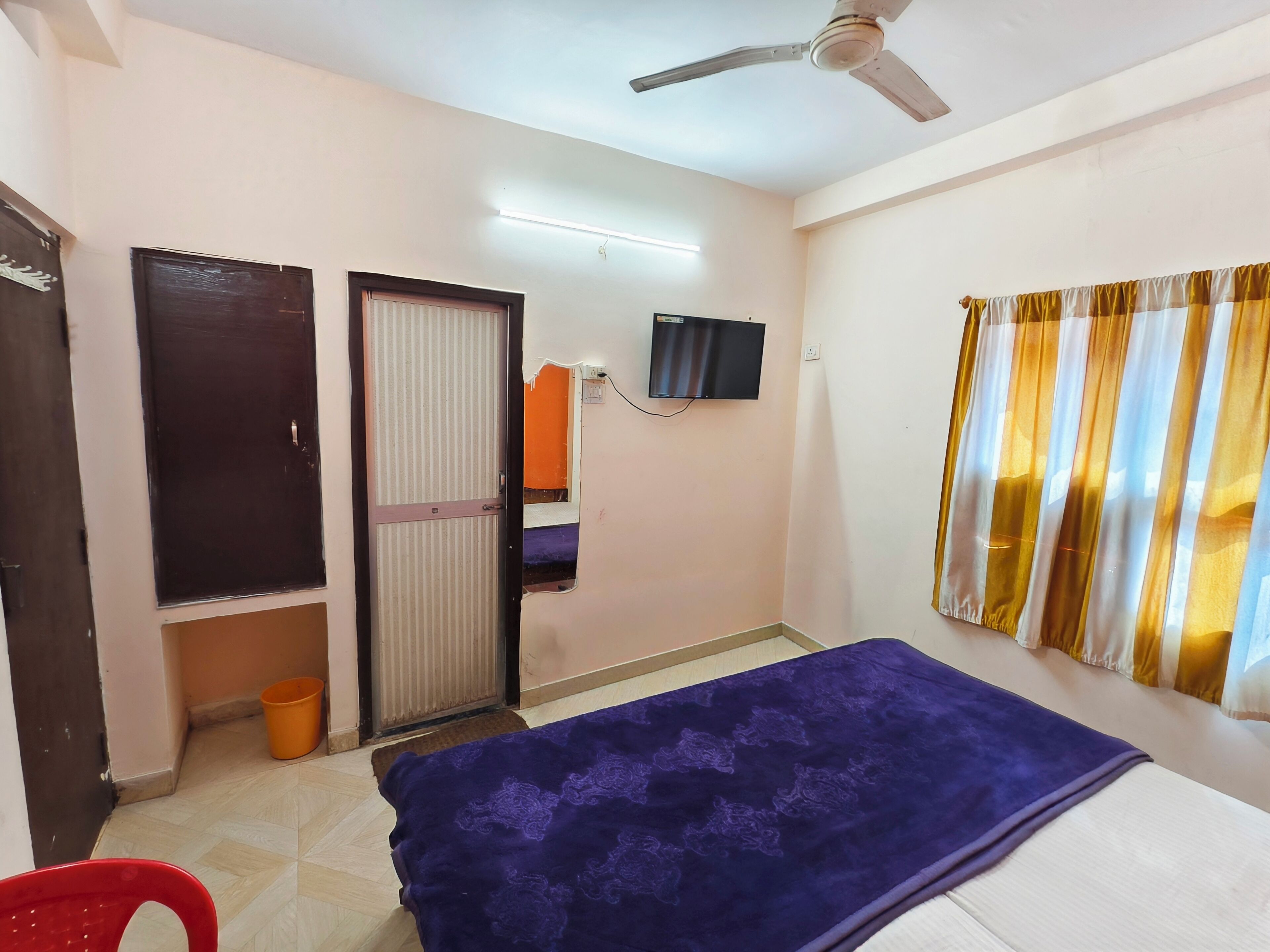 Un dormitorio con cama, ventilador de techo, televisor y ventana con cortinas.