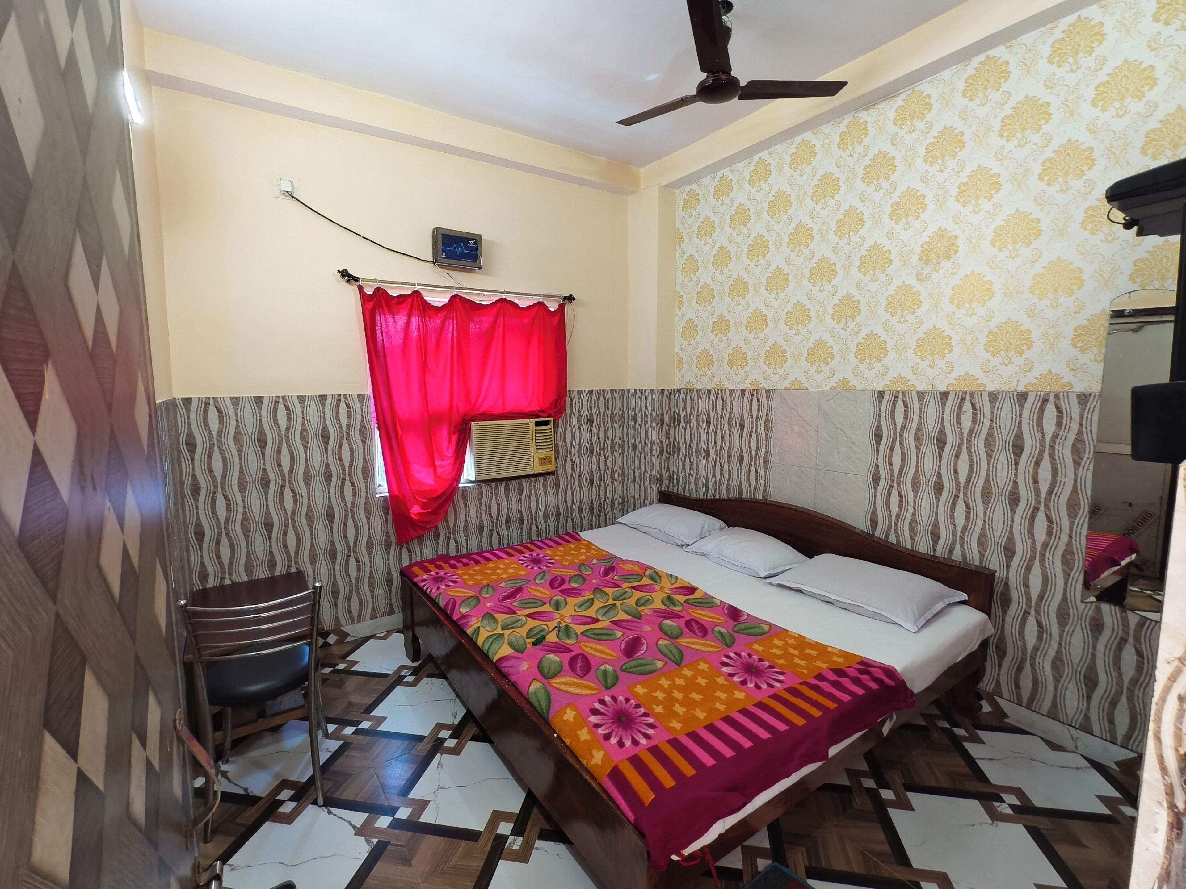 A bedroom with a bed, a ceiling fan, a wall-mounted air conditioner, and patterned wallpaper.