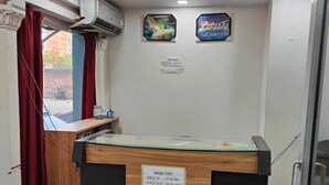 A hotel reception desk with a check-in/check-out sign, air conditioning units, and a wall with two framed pictures. - Hotel Vijay (Rajgir)