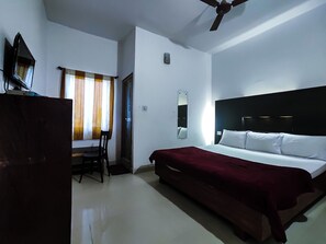 Une chambre d’hôtel équipée d’un lit, d’un bureau, d’une chaise, d’un ventilateur de plafond et d’une fenêtre avec des rideaux.