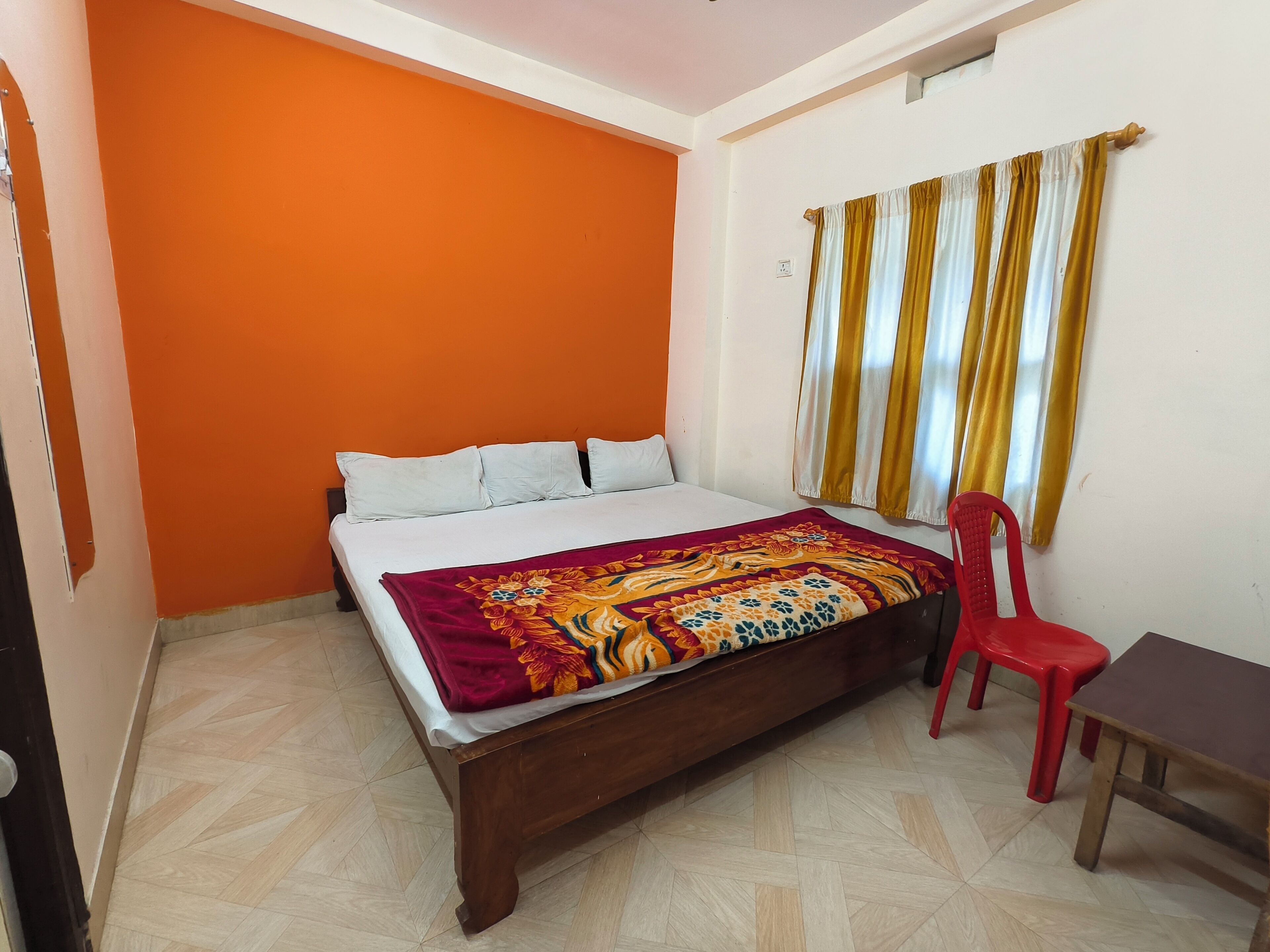 Une chambre avec un mur orange, un lit en bois, une chaise rouge et une petite table.