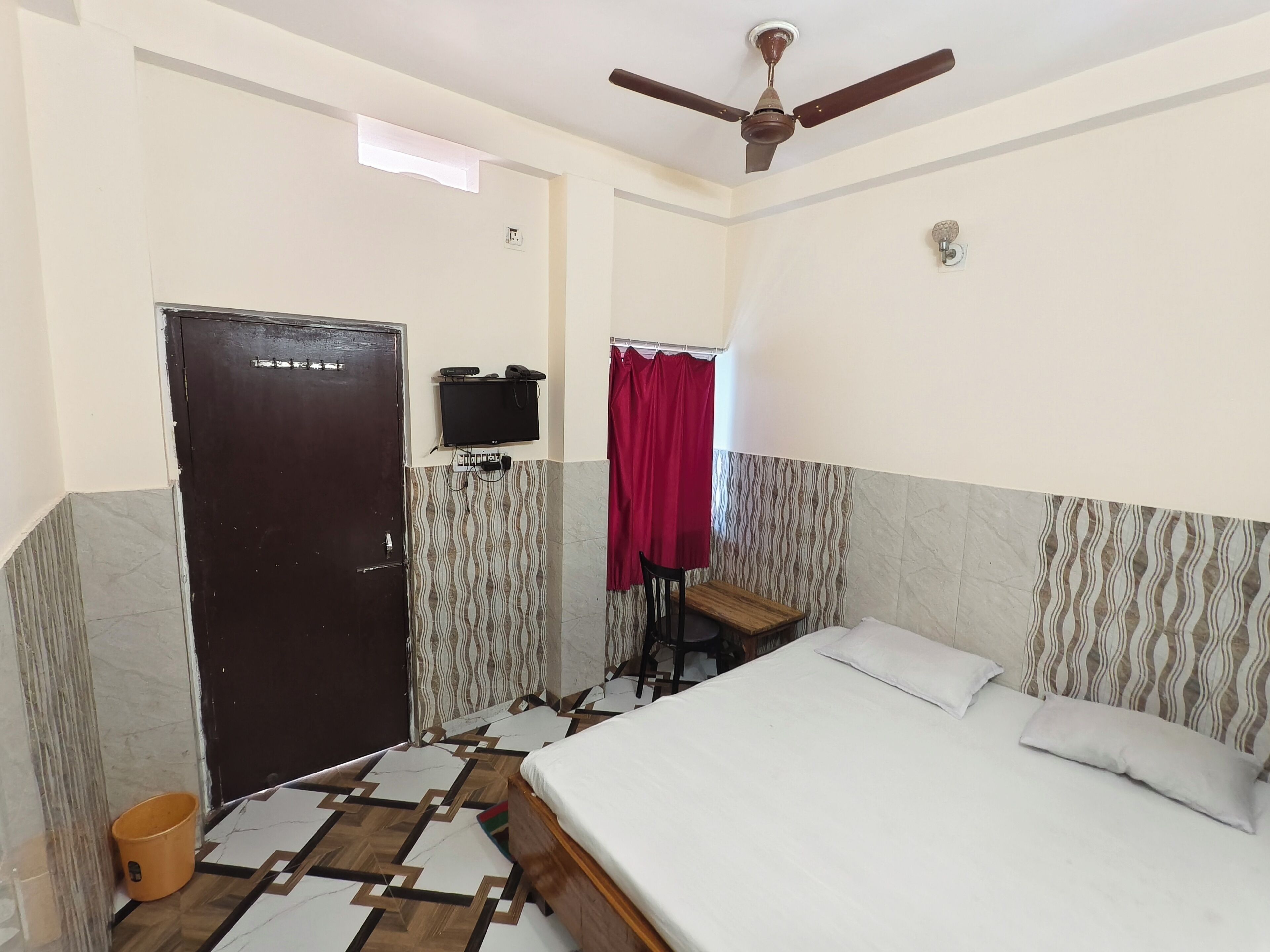A hotel room with a bed, a ceiling fan, a television, and a patterned floor.