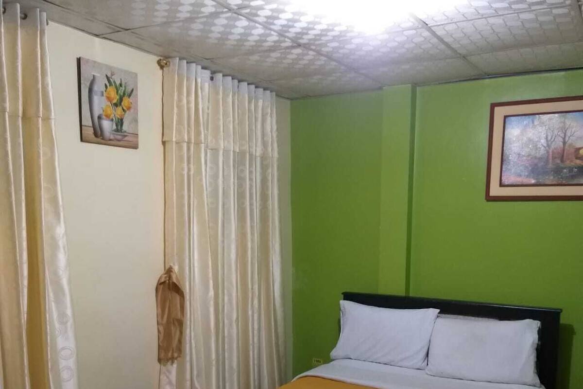 A room with a bed, green walls, a painting, and curtains.